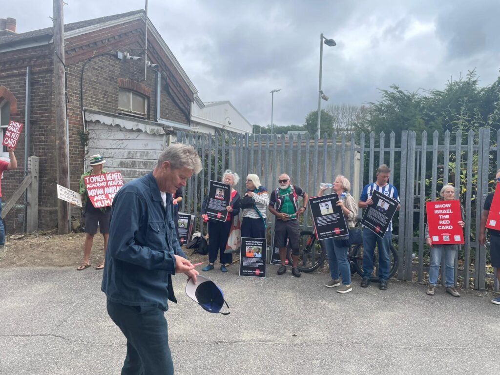 Seagulls Against Apartheid Show Israel The Red Card protest at Falmer Station. A man looks at an information card, while protesters hold placards demanding FIFA and UEFA Show Israel The Red Card. Photo Jathan Granger